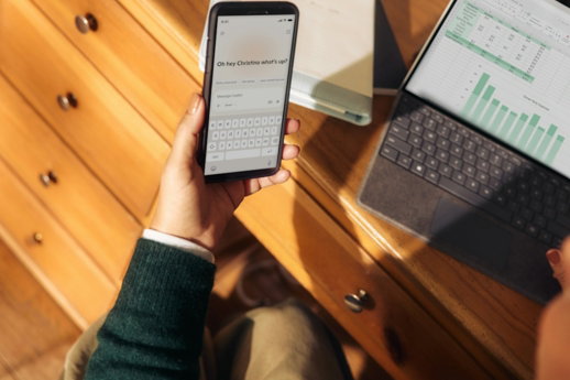person-holding-phone-near-laptop-and-tablet-on-desk.jpg Person holding phone near laptop and tablet on desk